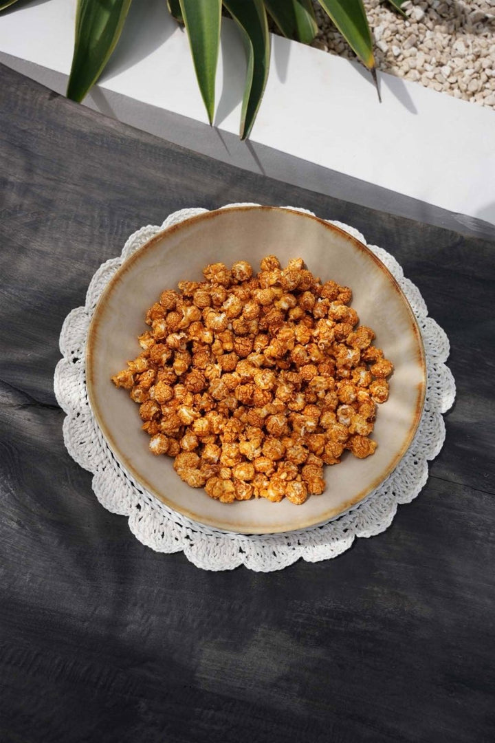 Bowl of popcorn on a textured surface with a plant in the background