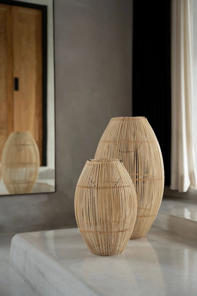 Two woven rattan vases on a reflective surface with a neutral background
