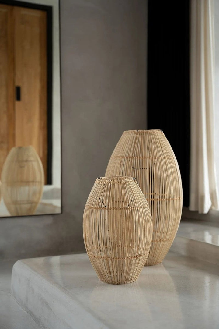 Two woven rattan vases on a reflective surface with a neutral background