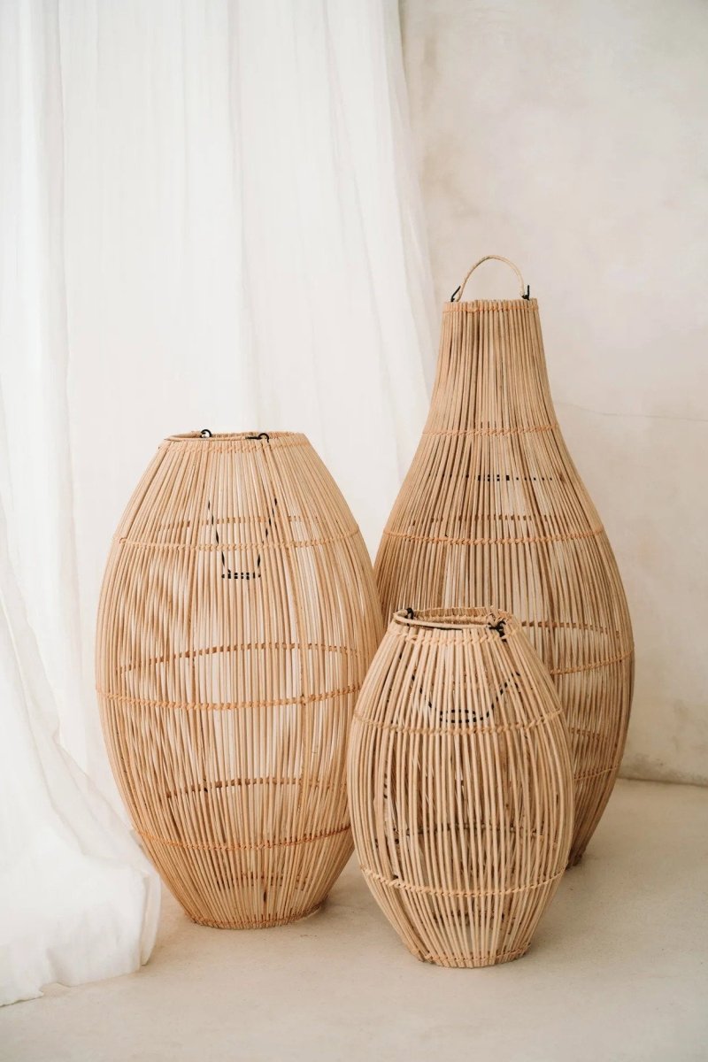 Three woven rattan vases of different sizes against a white curtain background
