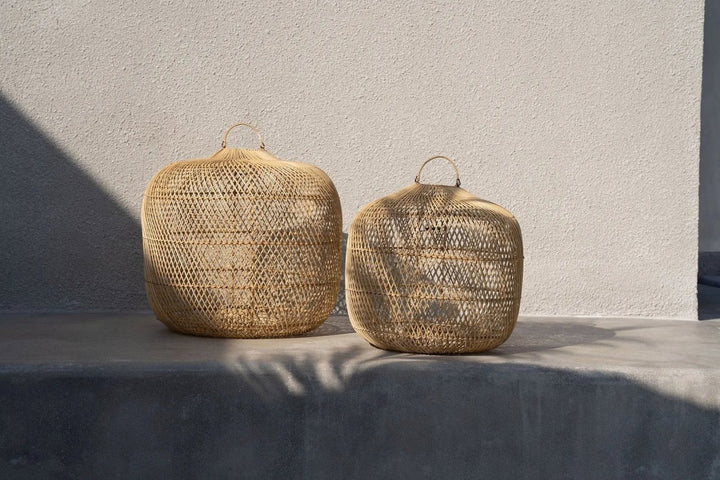 Two woven lamps on a concrete surface with a neutral background