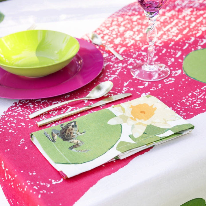 Table setting with a pink tablecloth, green bowl, purple plate, floral napkin, and glass.