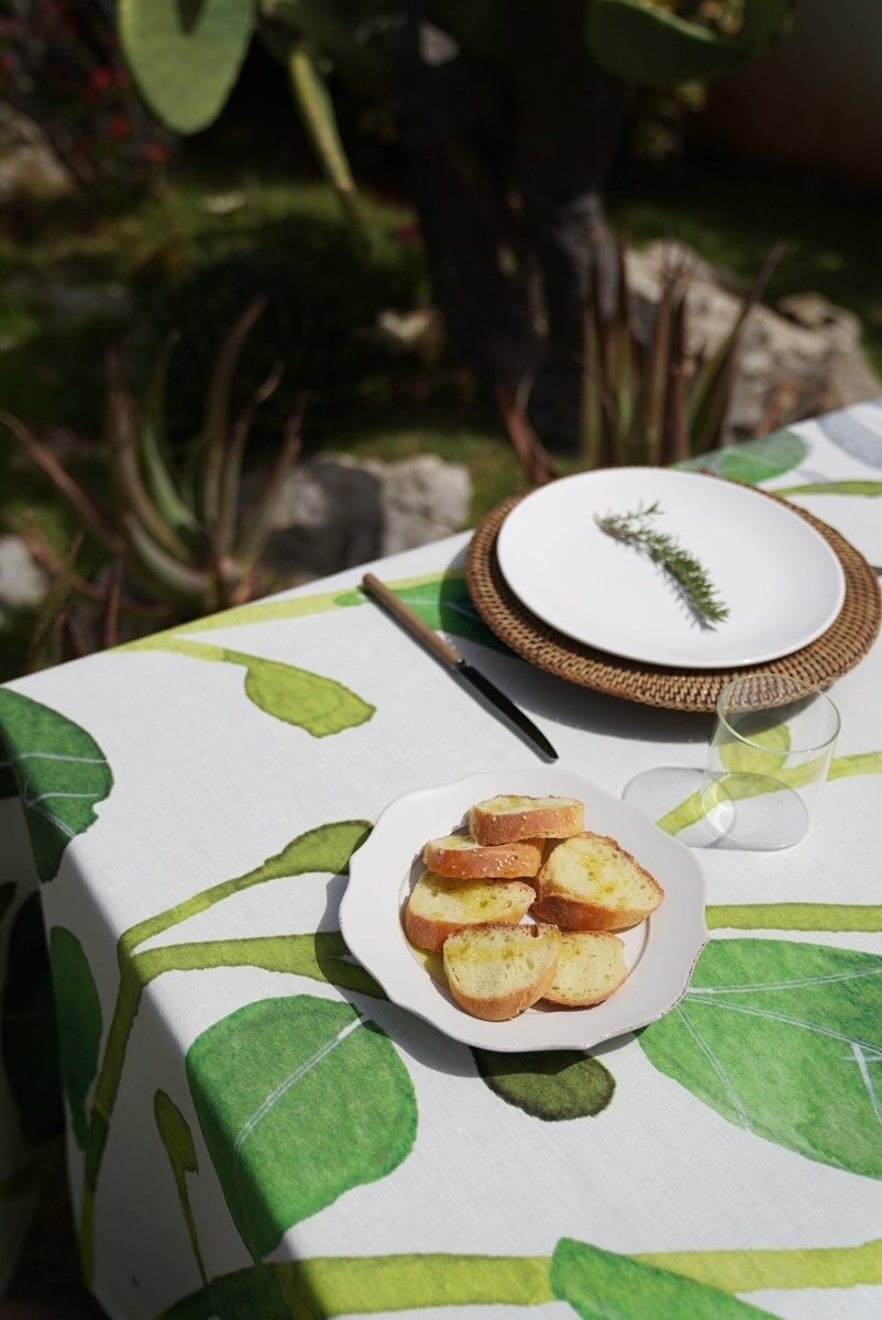 Table setting with plates of bread and a glass on a leaf-patterned tablecloth outdoors.
