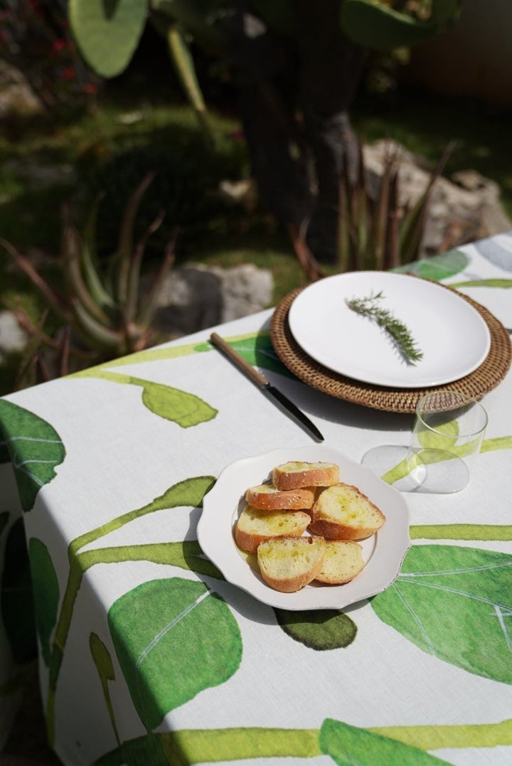 Table setting with plates of bread and a glass on a leaf-patterned tablecloth outdoors.