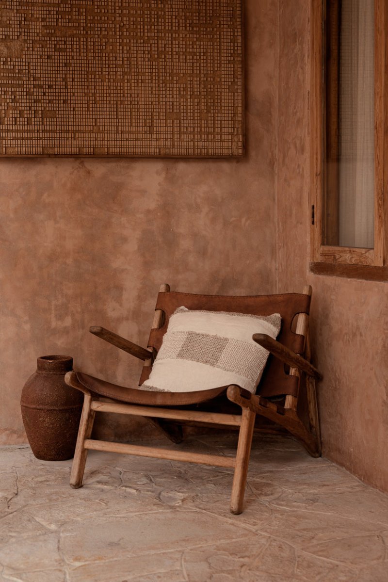 Wooden chair with a pillow against a textured wall.