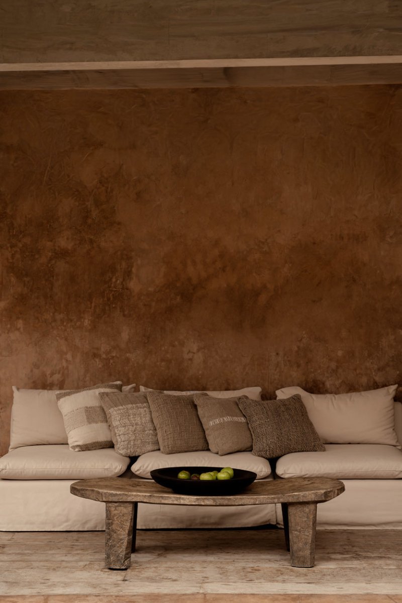 Beige sofa with patterned cushions against a brown textured wall.