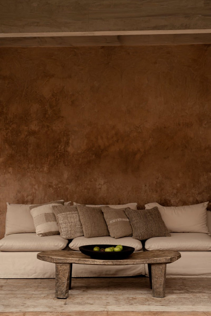 Beige sofa with patterned cushions against a brown textured wall.