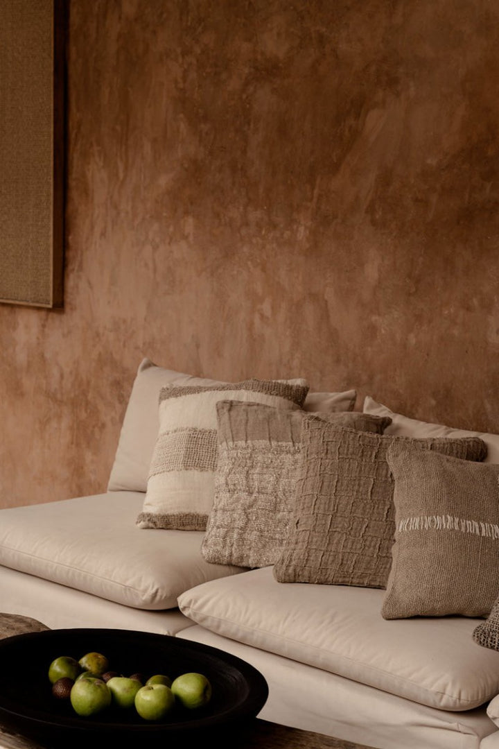 Beige sofa with textured pillows against a brown wall