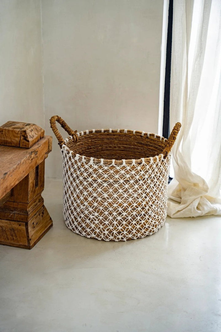 Woven basket on a white floor with a wooden side table and curtain in the background