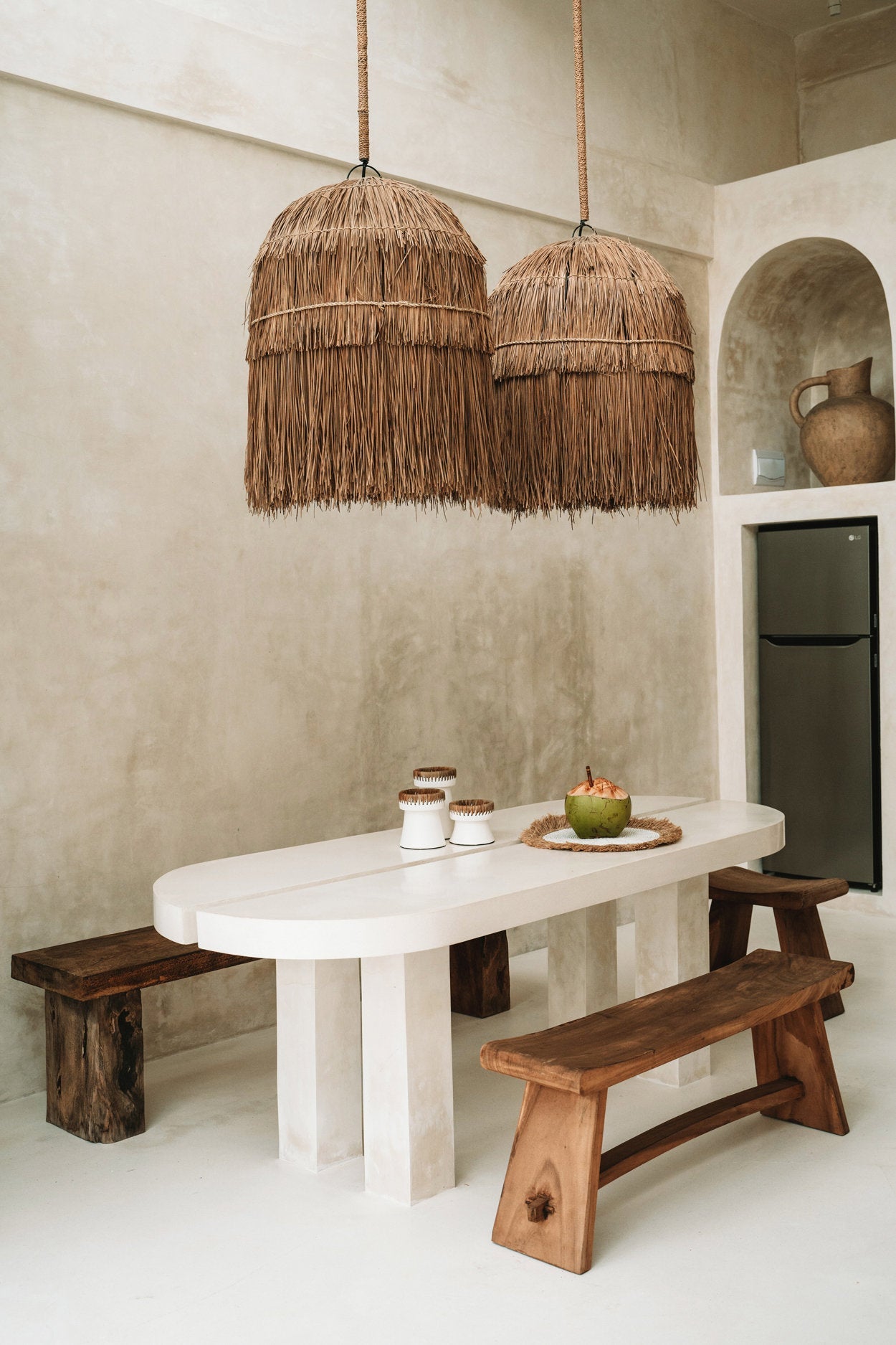 Dining area with a white table, wooden benches, and straw pendant lights.