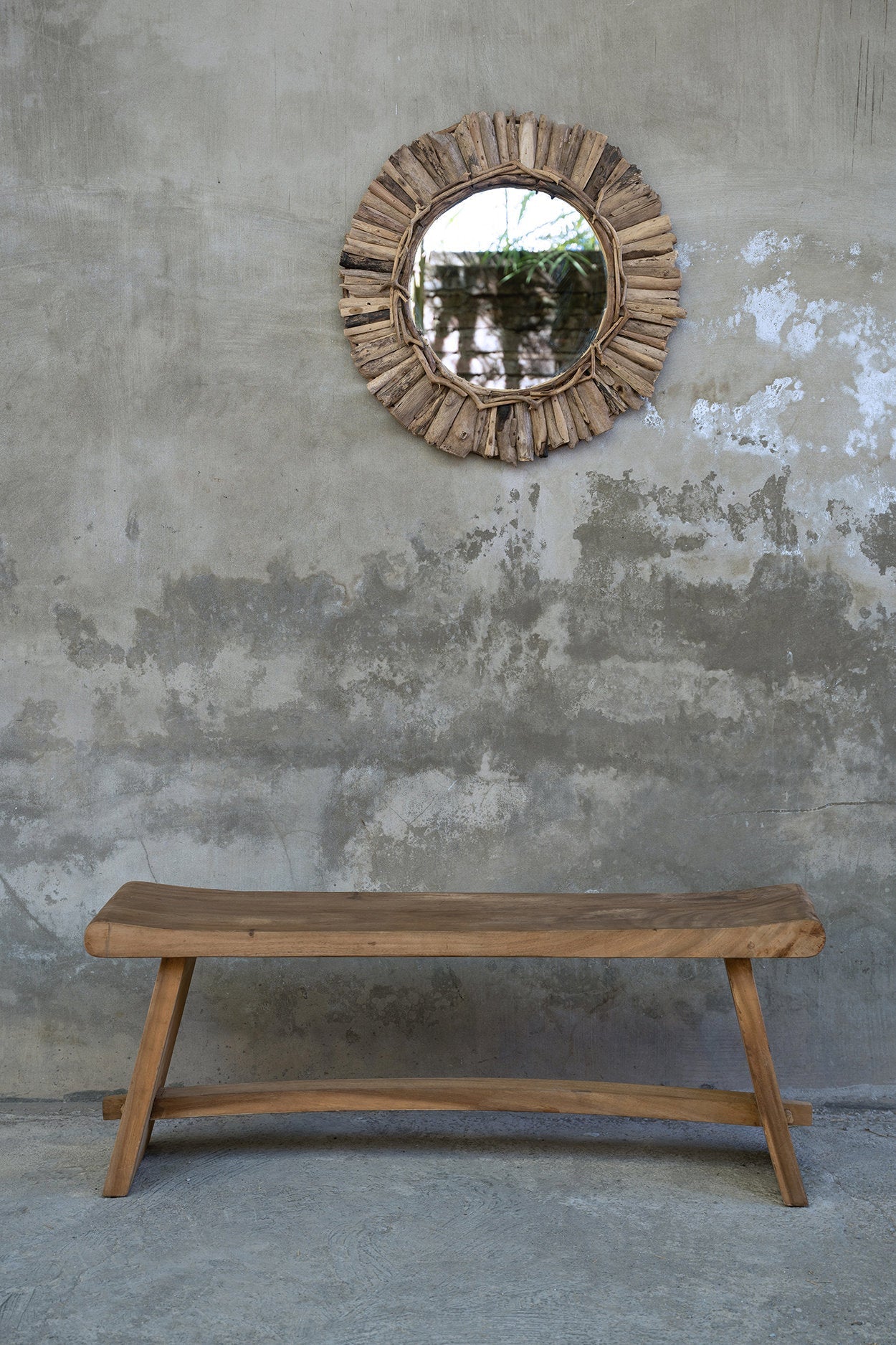 Wooden bench and round mirror with natural wood frame against a textured wall.