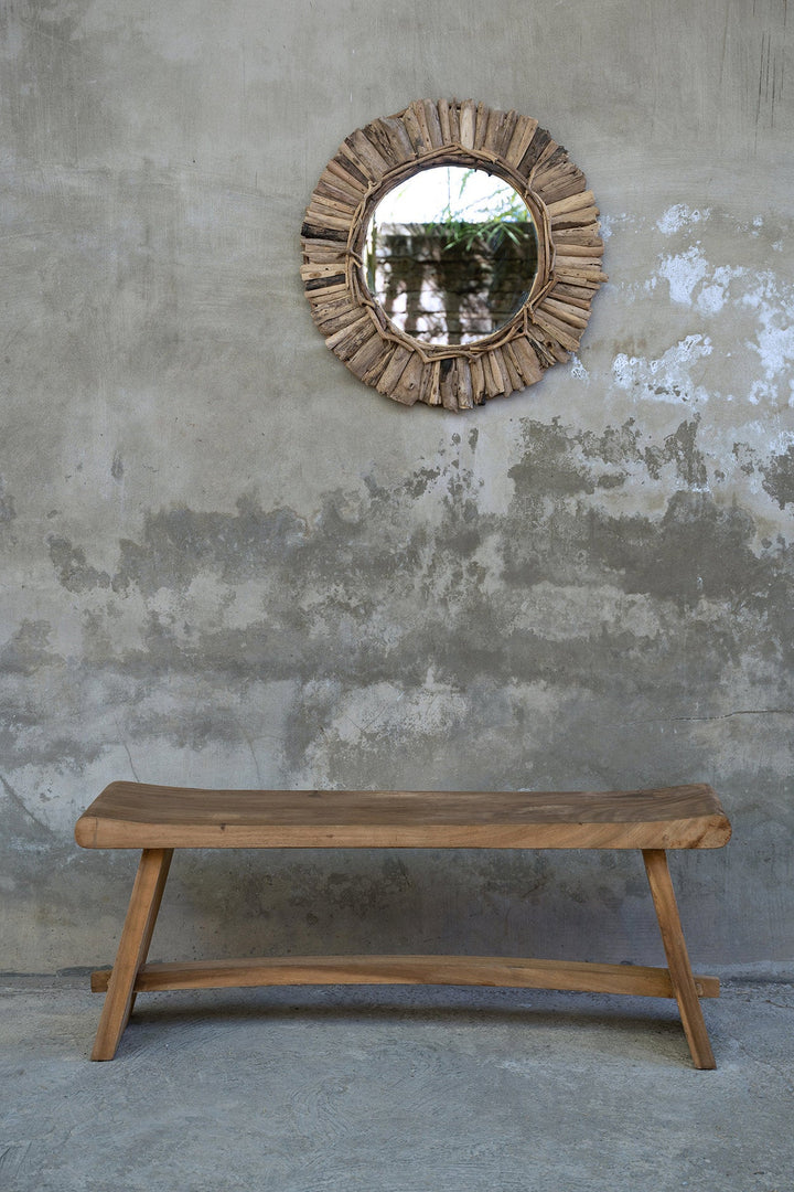 Wooden bench and round mirror with natural wood frame against a textured wall.