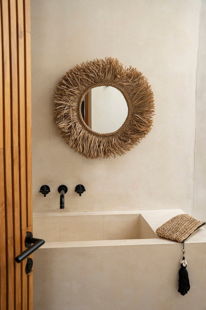 Bathroom with a round woven mirror above a bathtub.
