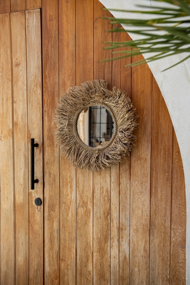 Round woven mirror on a wooden door with a plant in the corner