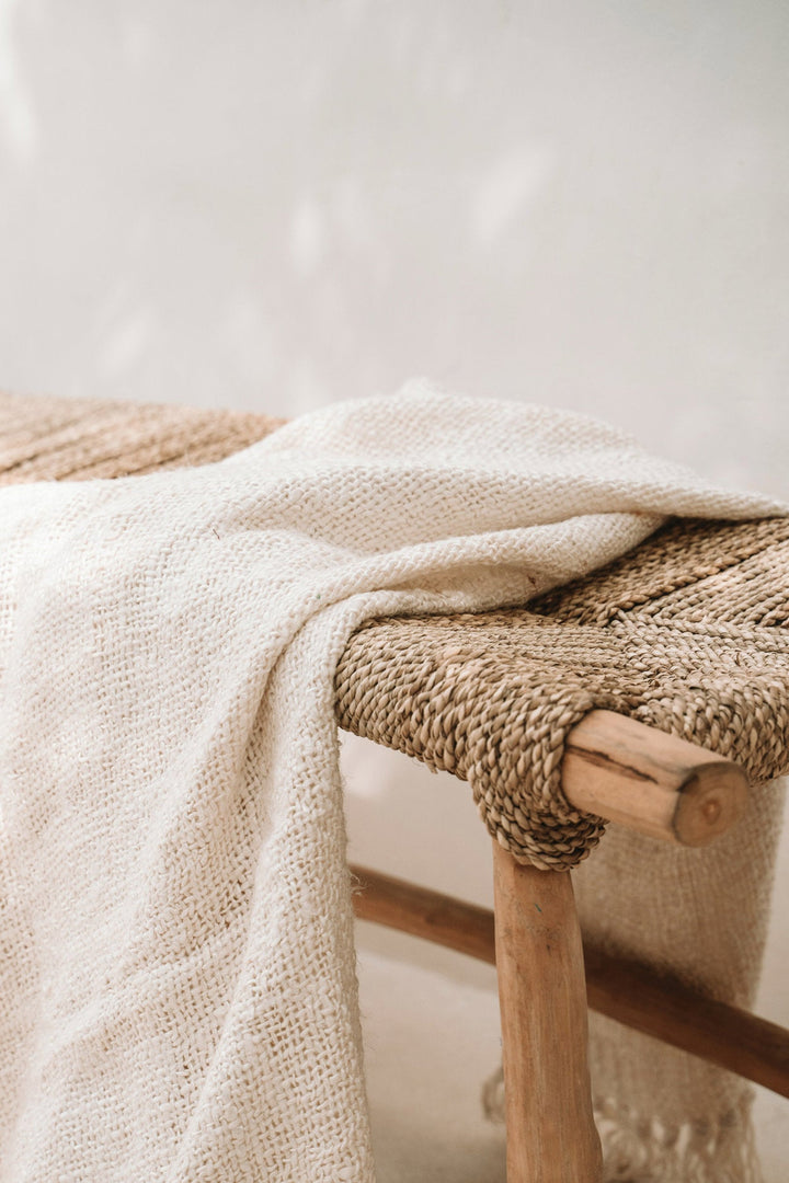 Beige textured blanket draped over a woven chair with a neutral background