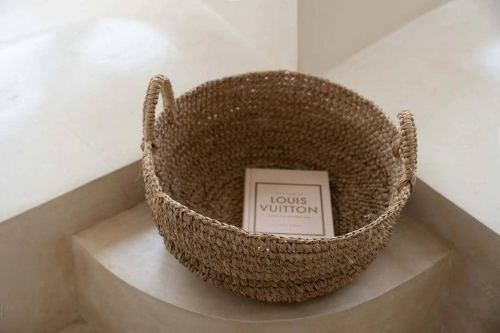 Woven basket with a Louis Vuitton box inside on a light surface