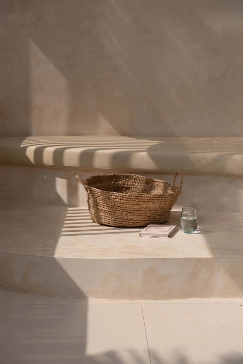 Wicker basket on a stone surface with a glass of water, against a neutral wall.