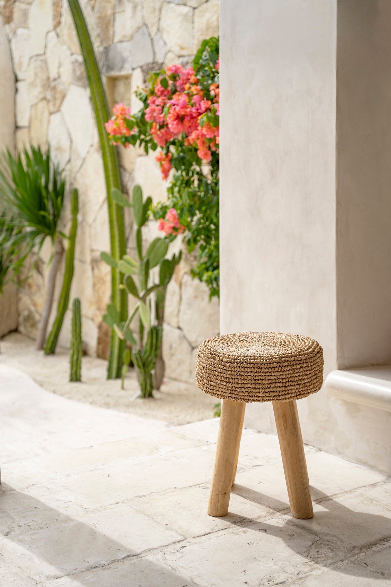 Woven stool on a stone patio with plants and flowers in the background