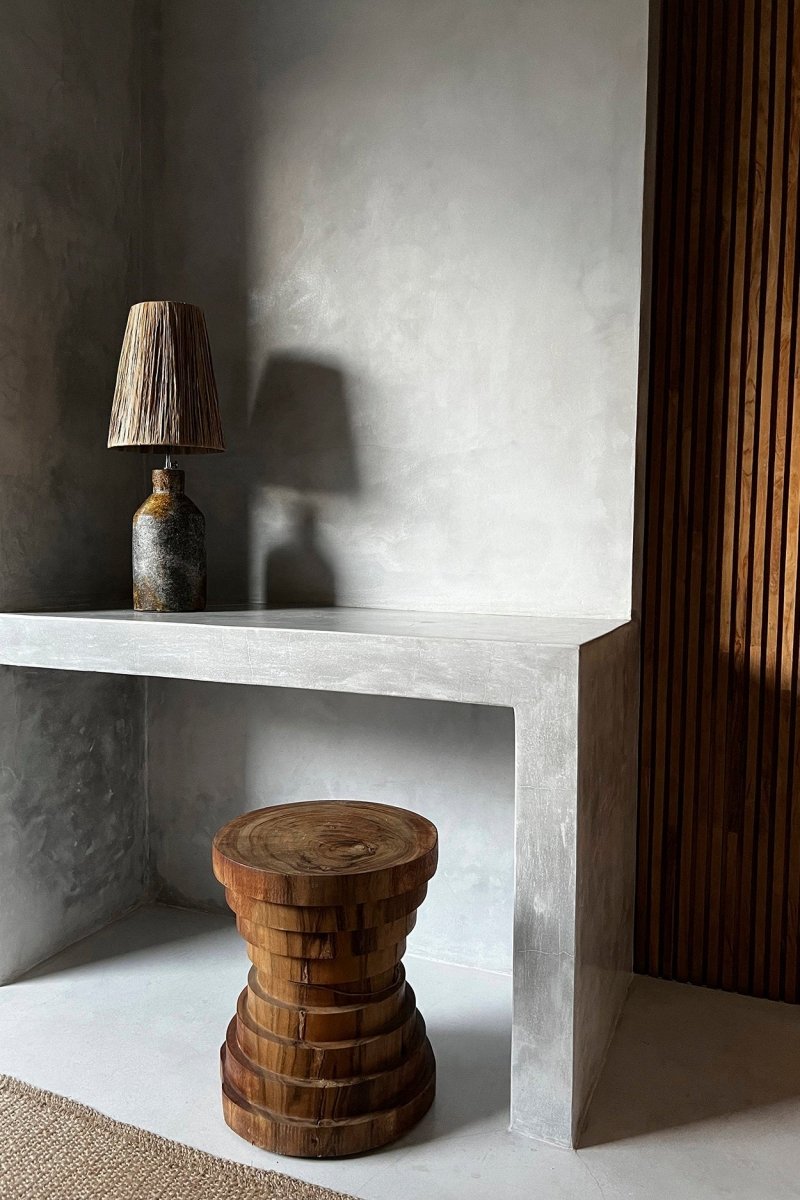 Wooden stool and lamp on a concrete shelf against a textured wall.