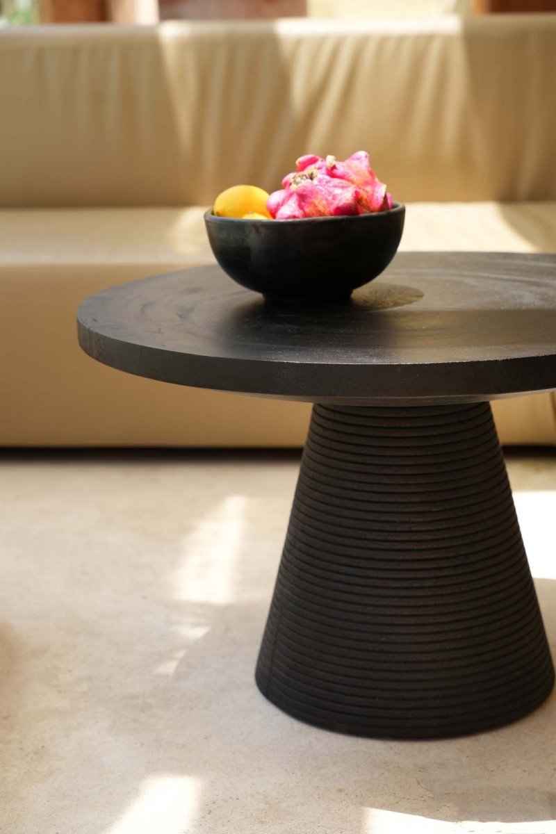 Black round table with a bowl of fruit on a light-colored floor.