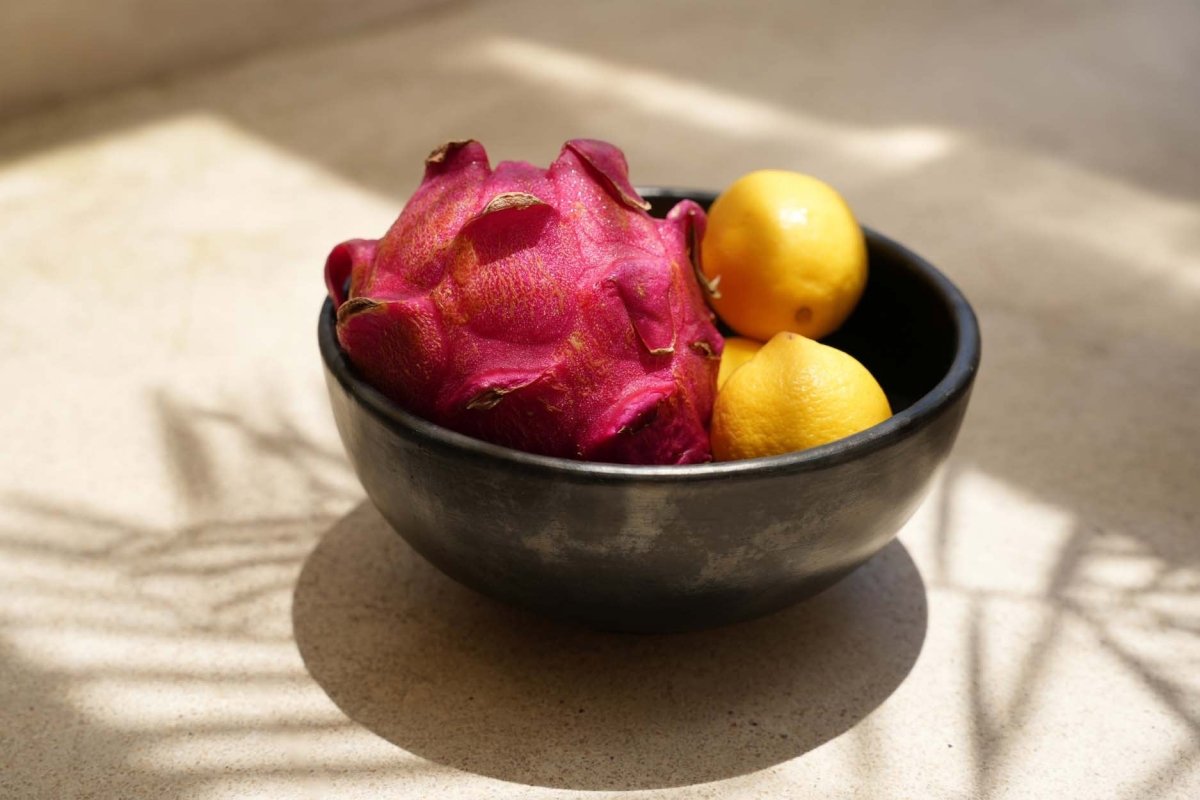 Black bowl with dragon fruit and lemons on a textured surface