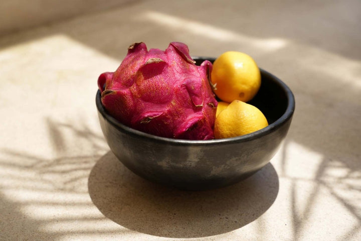 Black bowl with dragon fruit and lemons on a textured surface