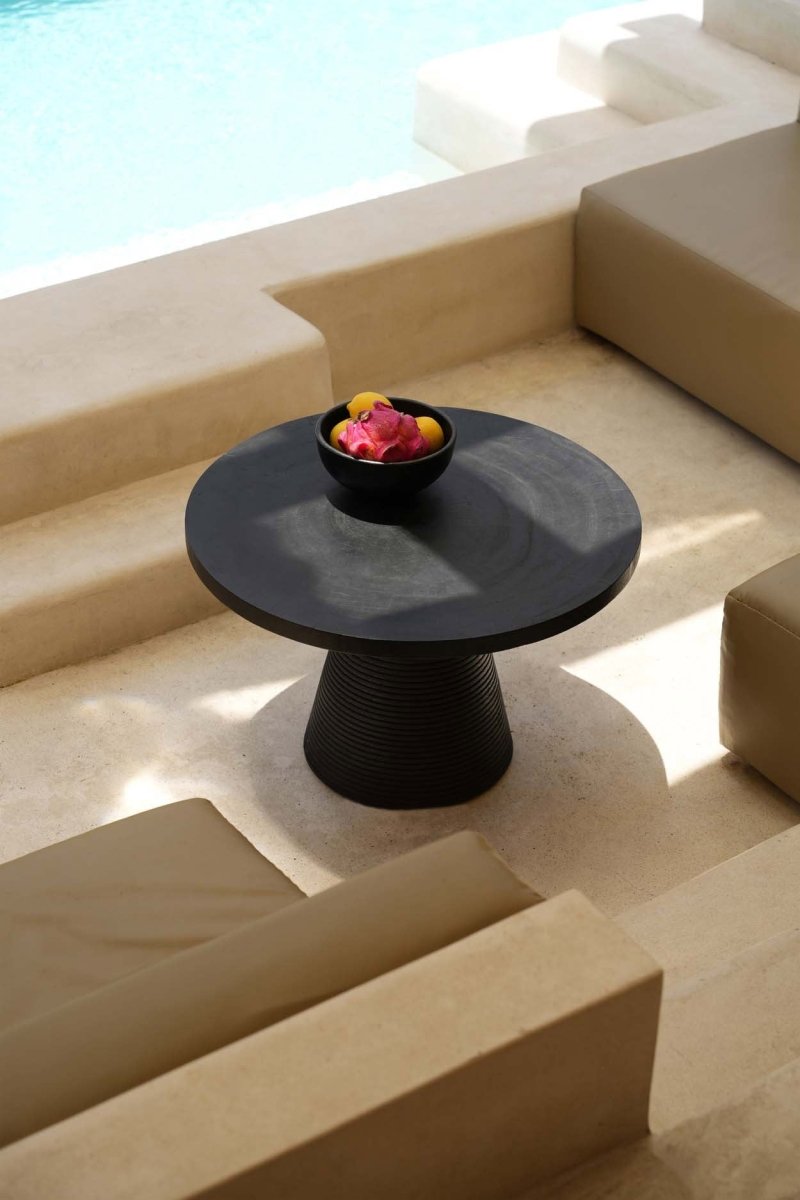 Black round table with fruit on a beige outdoor staircase near a pool