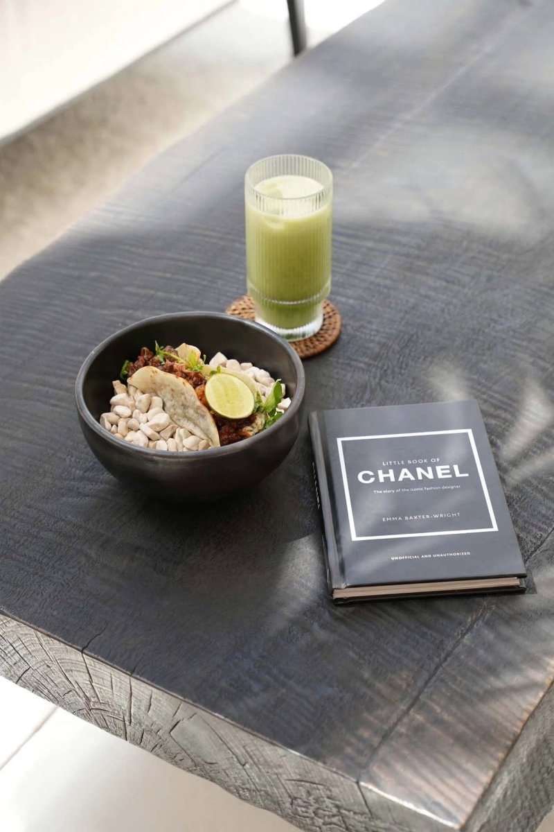 Bowl of food, glass of green juice, and Chanel book on a dark surface