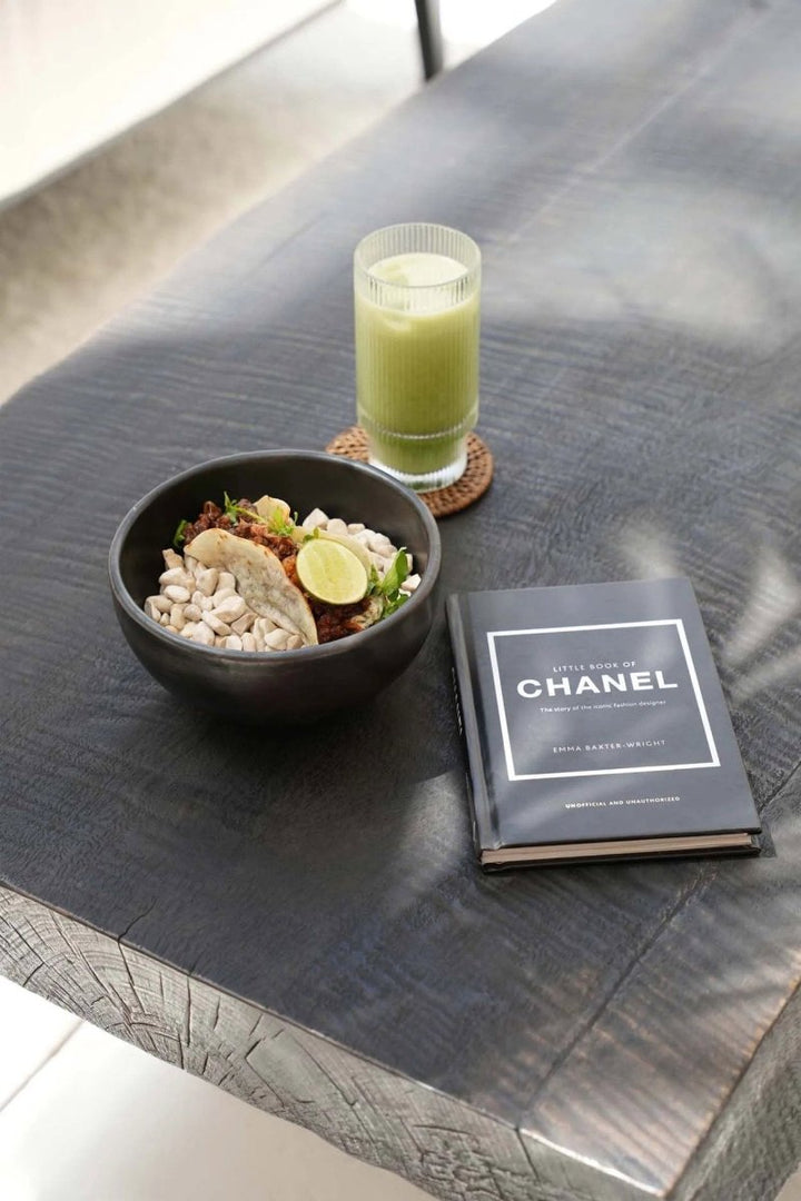 Bowl of food, glass of green juice, and Chanel book on a dark surface