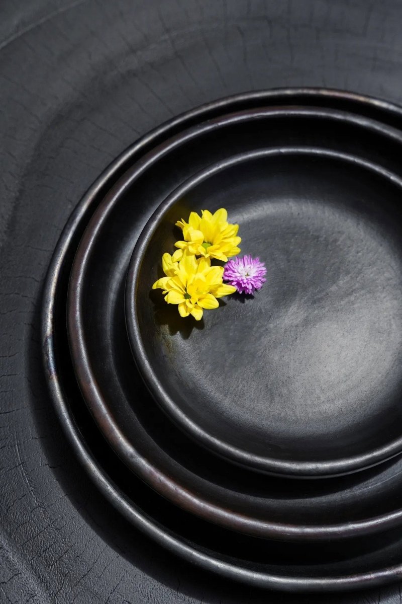 Three black plates stacked with two flowers on the topmost plate.