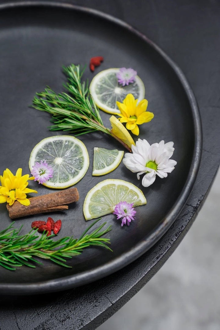 Decorative arrangement of lime slices, flowers, and herbs on a black plate.