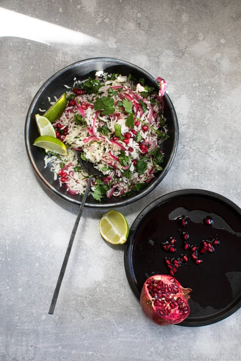 Salad with pomegranate, lime, and mint in a black bowl on a gray surface.