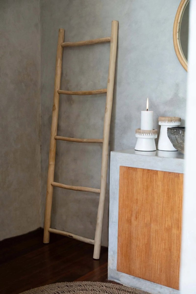 Wooden ladder leaning against a gray wall next to a wooden cabinet with decorative items.