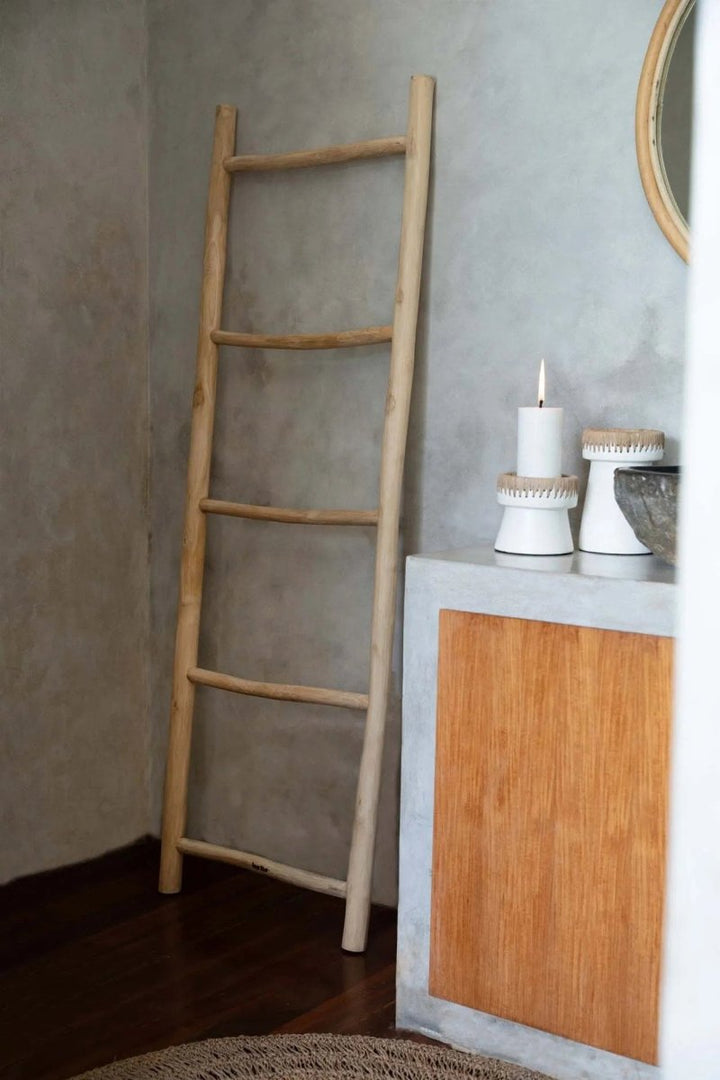 Wooden ladder leaning against a gray wall next to a wooden cabinet with decorative items.