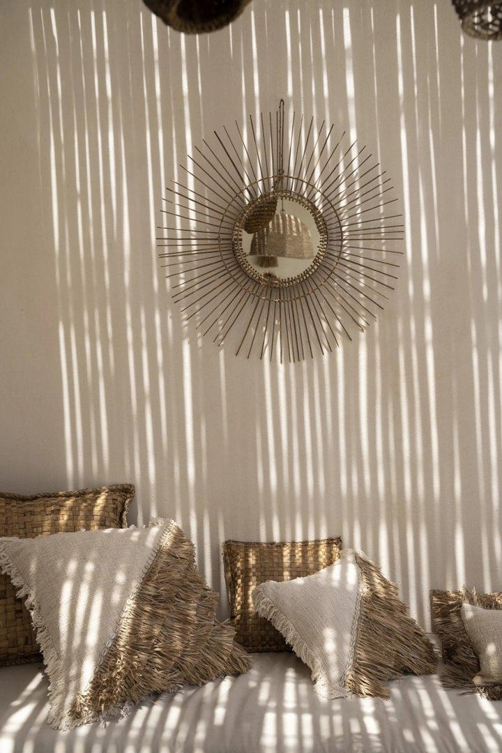 Decorative mirror with sunburst design on a wall with sunlight casting shadows.