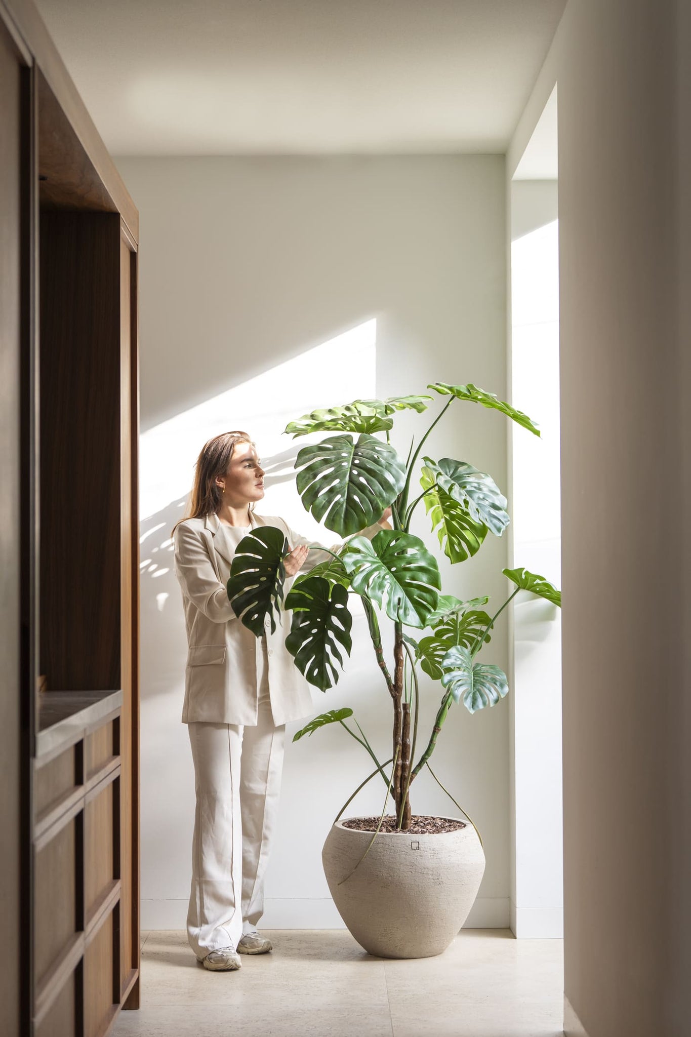 Person standing next to a large potted plant in a bright room