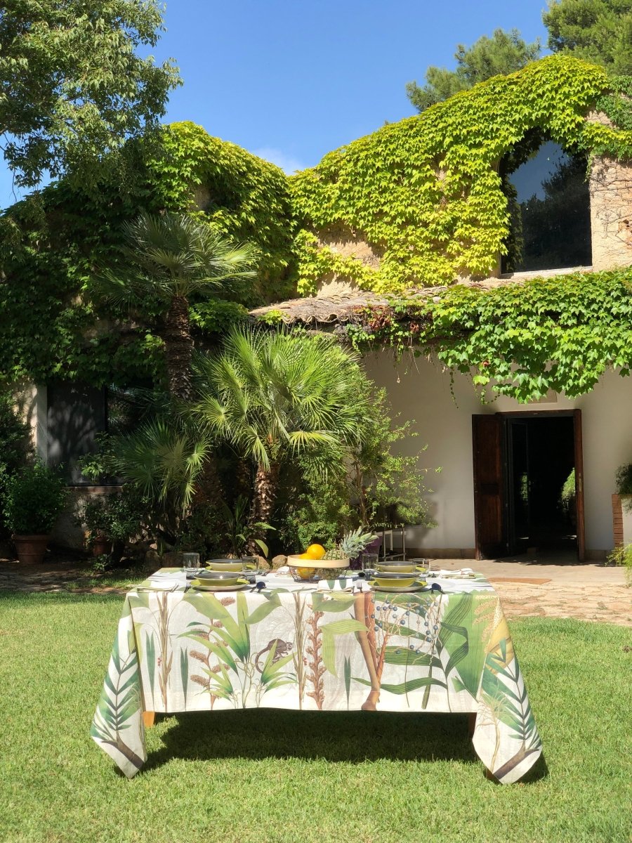 Table with a decorative tablecloth in a garden setting with a building and trees in the background.
