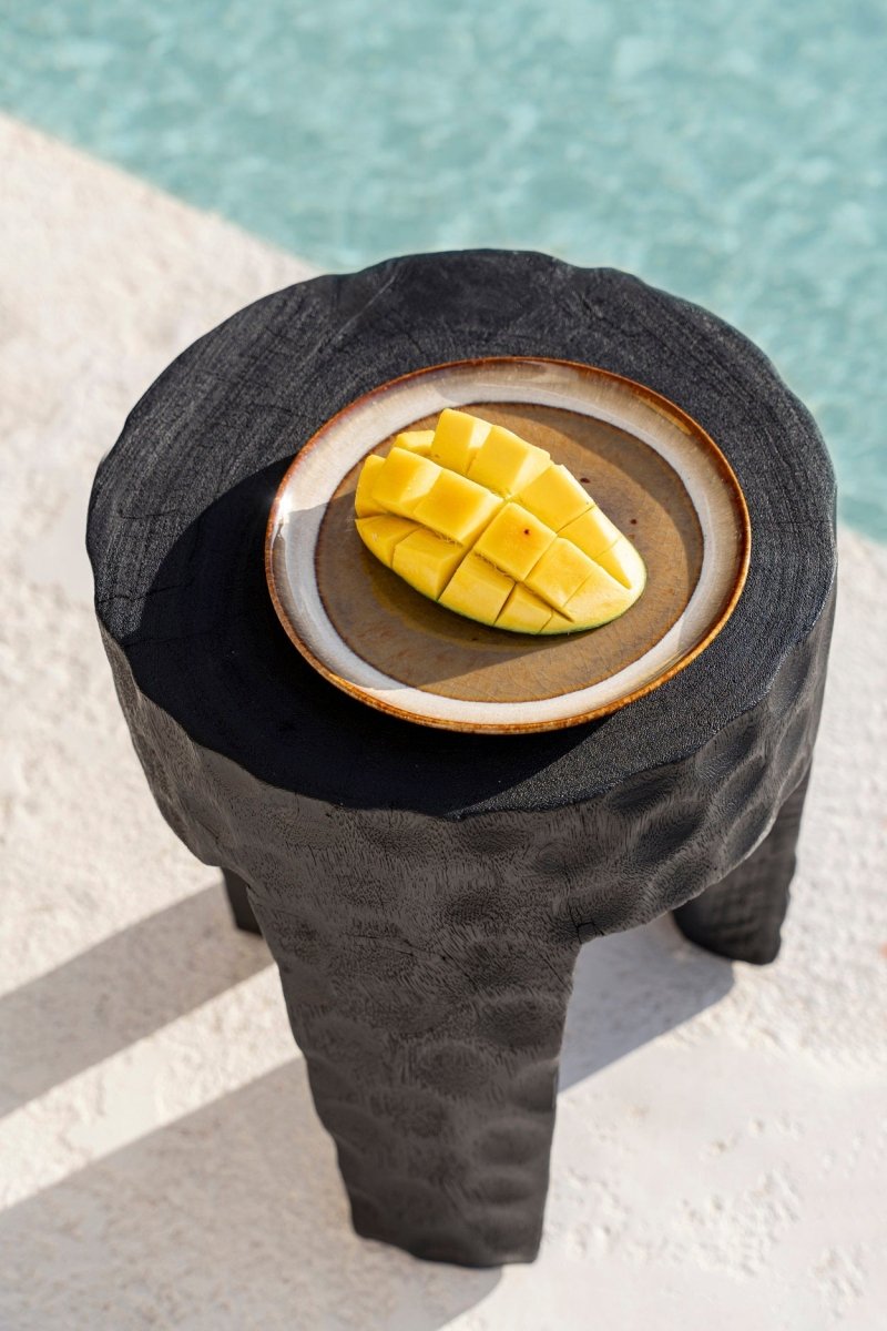 Mango slices on a wooden plate with a textured black stand by a poolside.