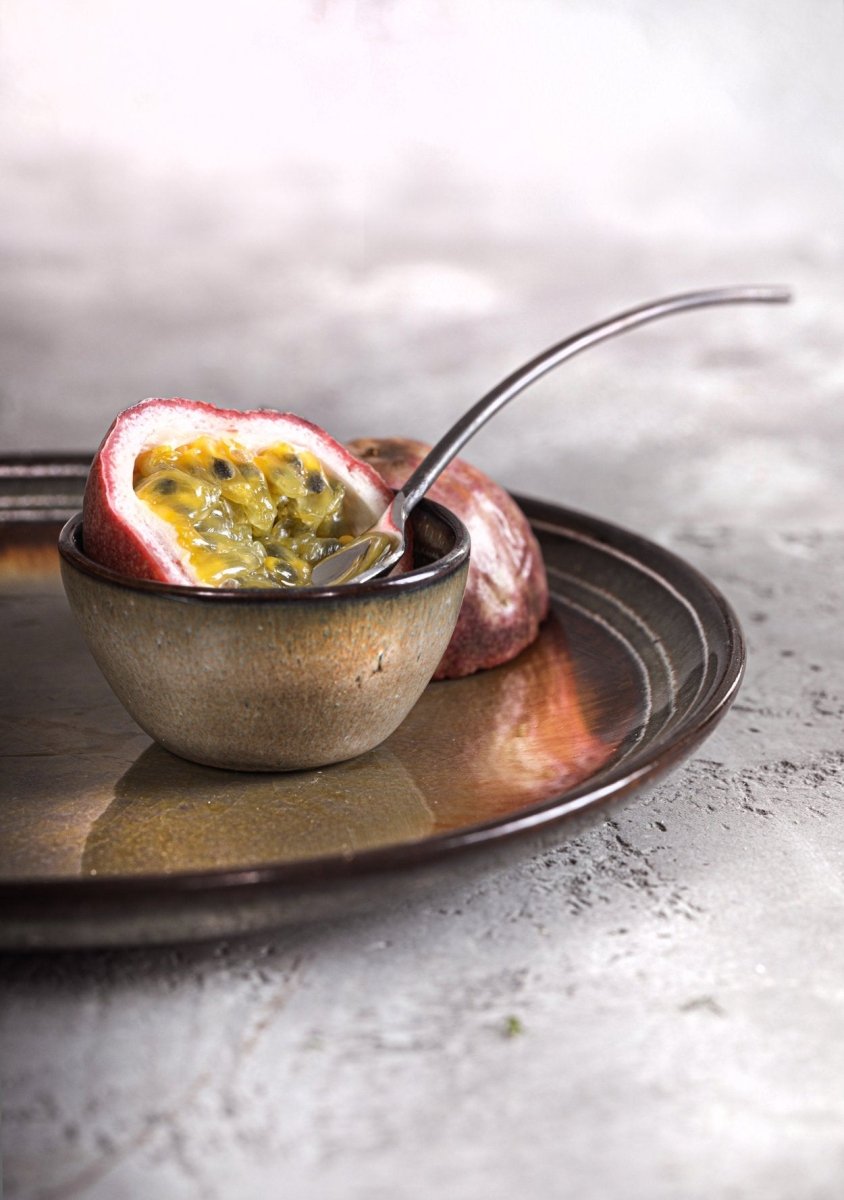 Passion fruit cut in half with a spoon on a textured plate