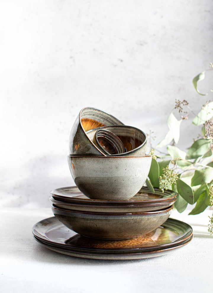 Set of ceramic bowls and plates on a light background with greenery