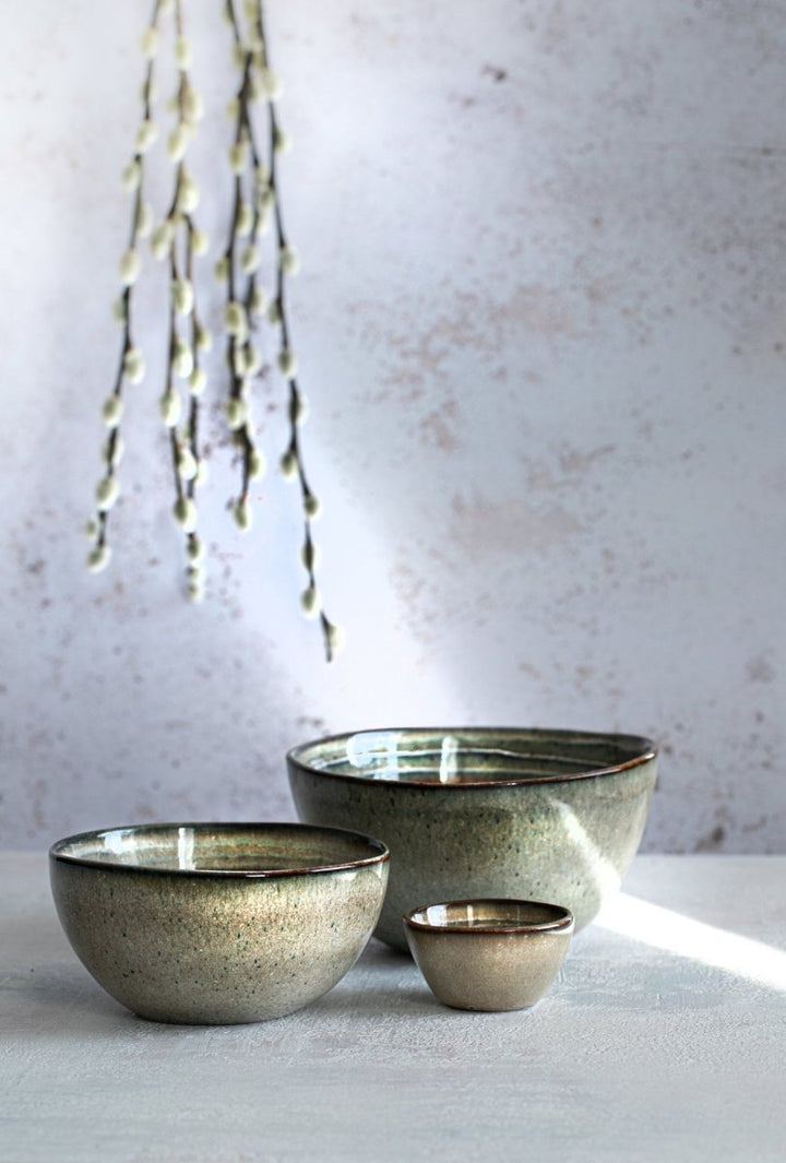 Three ceramic bowls of varying sizes on a light surface with a textured wall background.