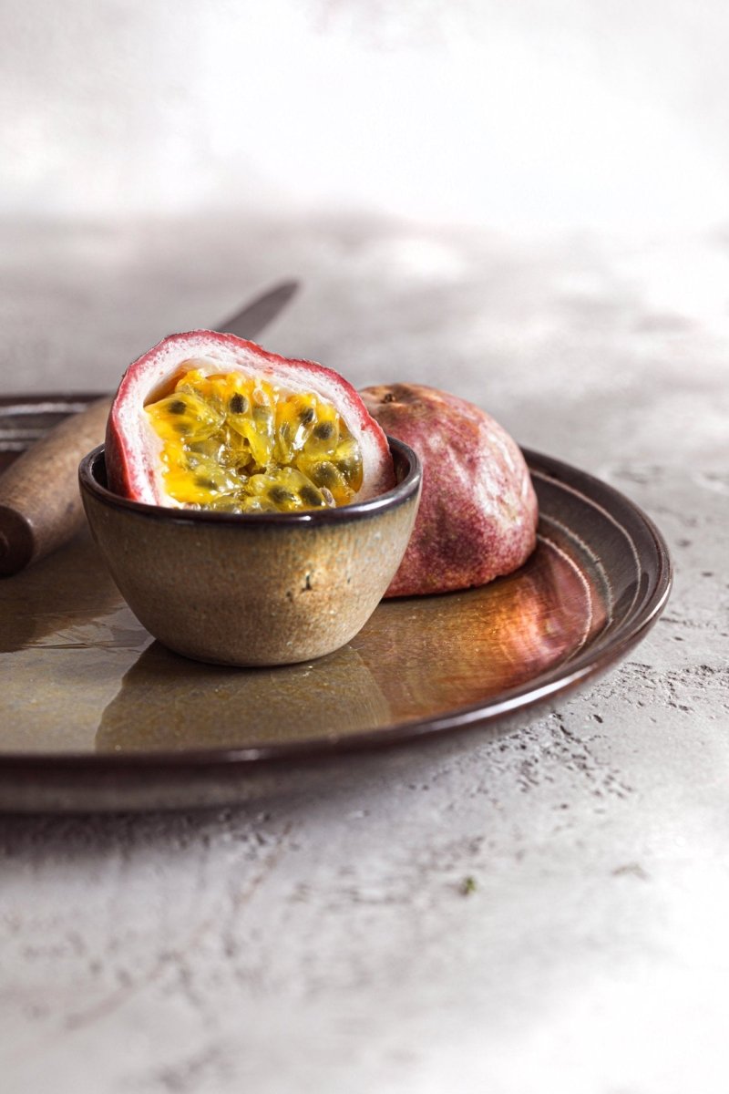 Halved passion fruit in a small bowl on a stone surface