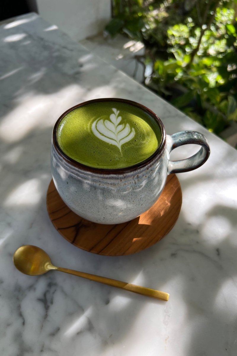 Cup of green matcha with latte art on a marble surface with a gold spoon.