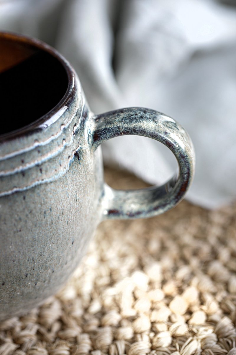 Close-up of a ceramic mug with a textured handle on a surface with scattered oats.
