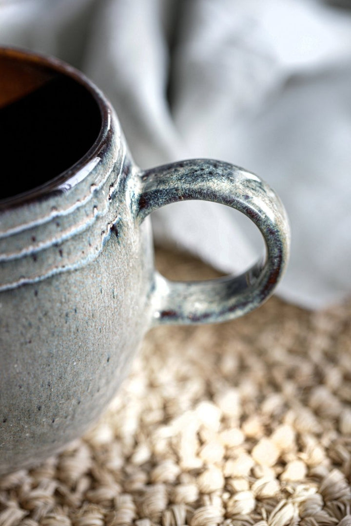 Gray ceramic mug on a textured surface with a blurred background