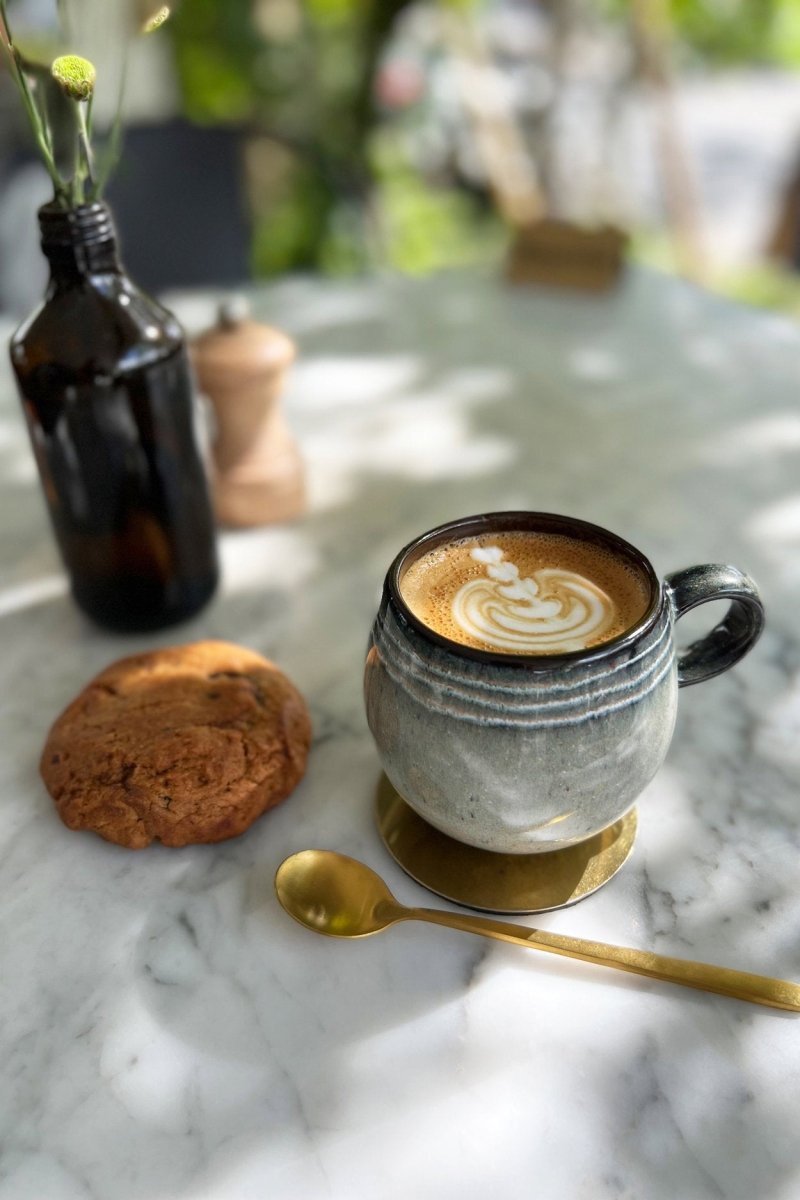 Cappuccino in a textured mug with a cookie and spoon on a marble surface