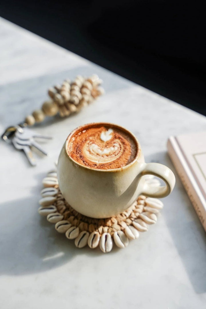 Cappuccino in a white mug on a textured coaster with a blurred background