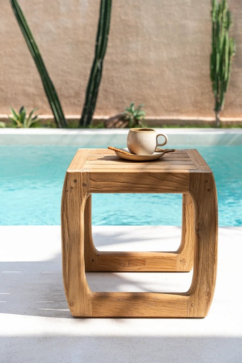 Wooden side table with a cup and saucer by a poolside