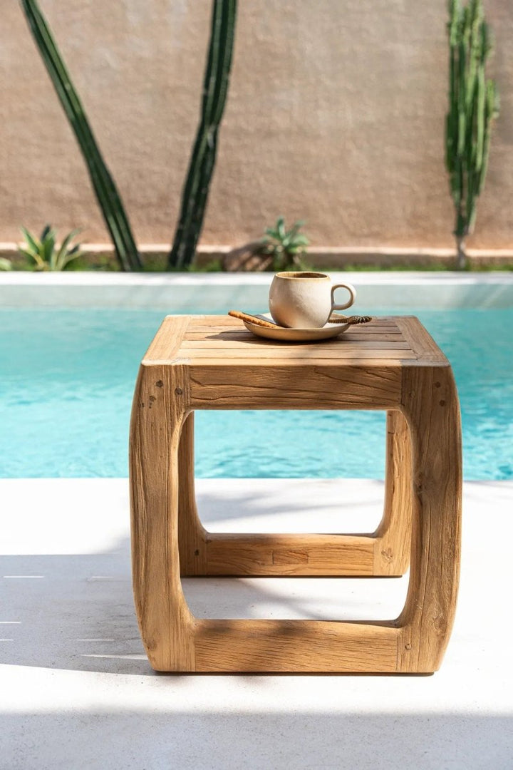 Wooden side table with a cup and saucer by a poolside