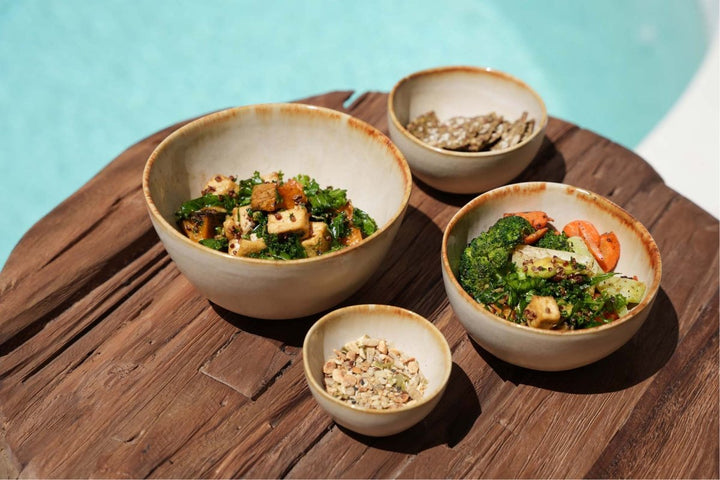 Four bowls of salad on a wooden table with a pool in the background